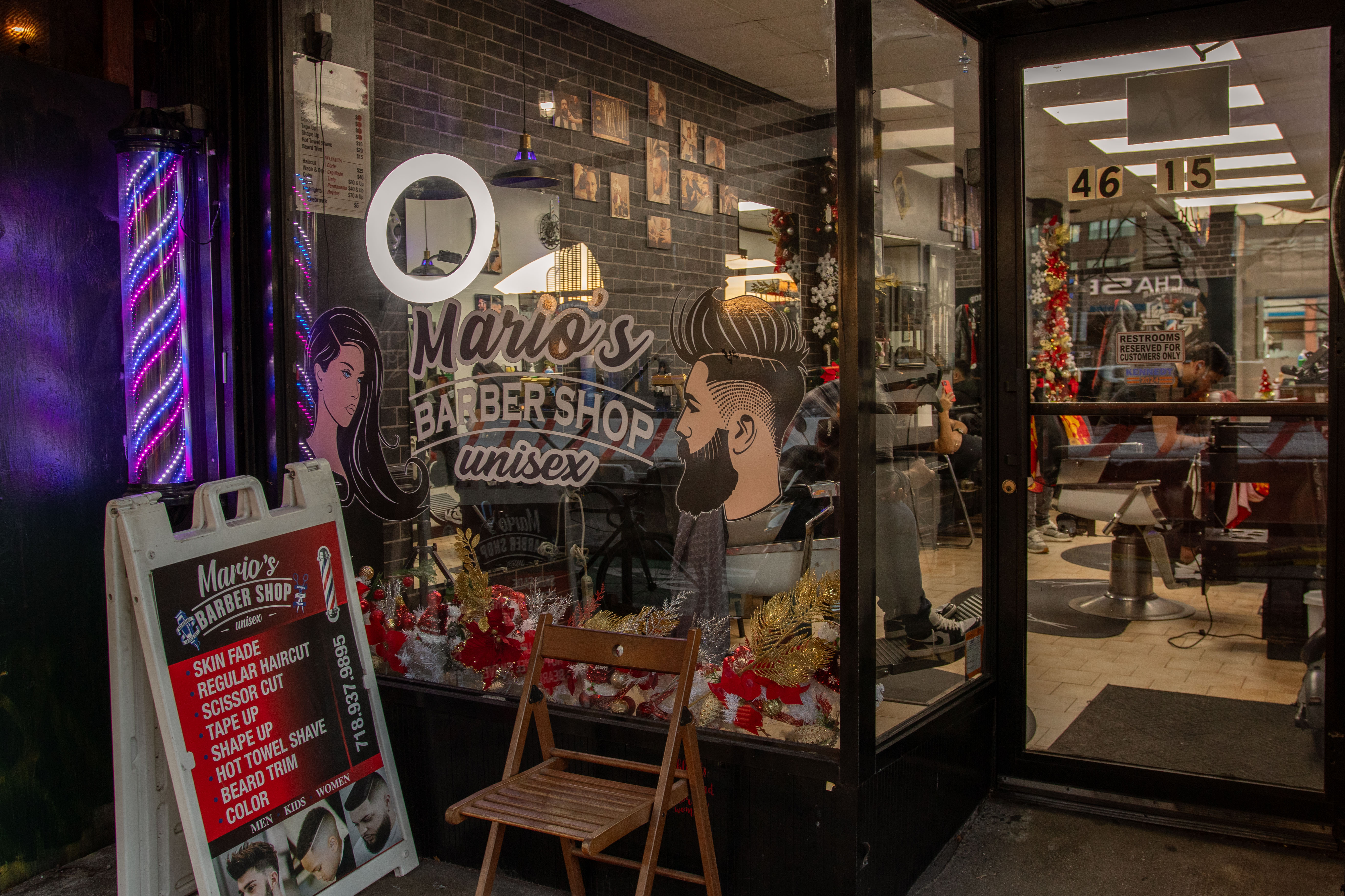 Exterior view of Mario's Barbershop showcasing a sign and a barber pole, with festive decorations visible in the window.